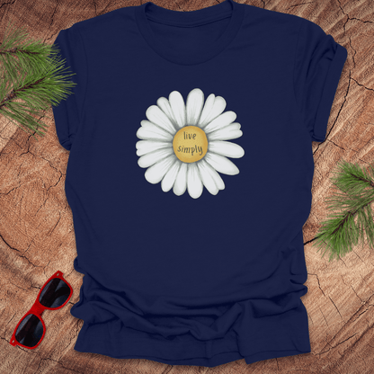 Navy blue t-shirt with a white flower graphic and 'live simply' text on a wooden surface with sunglasses and greenery.