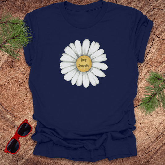 Navy blue t-shirt with a white flower graphic and 'live simply' text on a wooden surface with sunglasses and greenery.