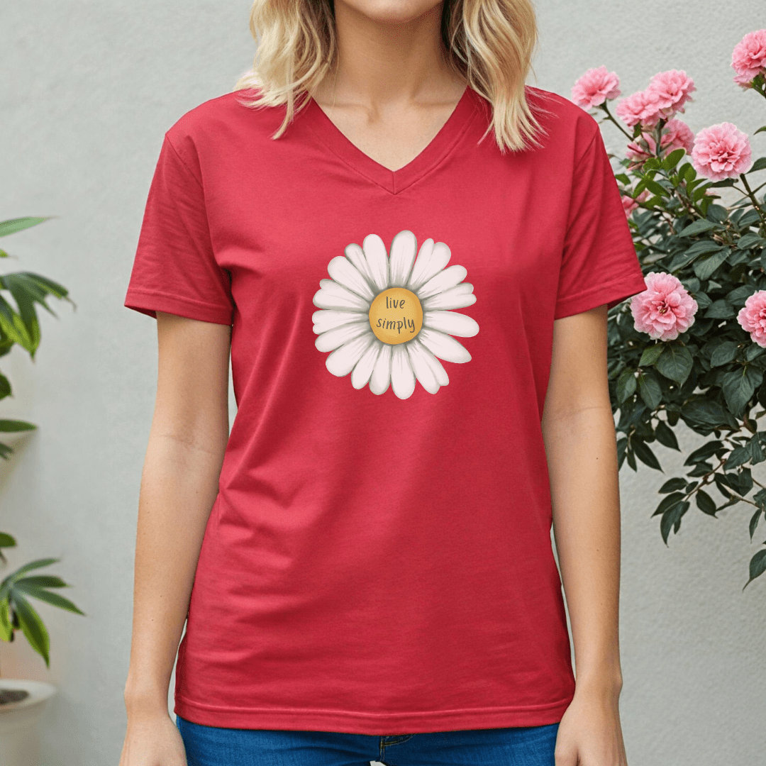 Person wearing a red v-neck t-shirt with a white flower graphic and 'Live Simply' text, standing in front of pink flowers.