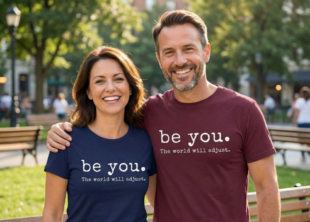 Two people wearing 'be you. the world will adjust.' t-shirts in a park setting