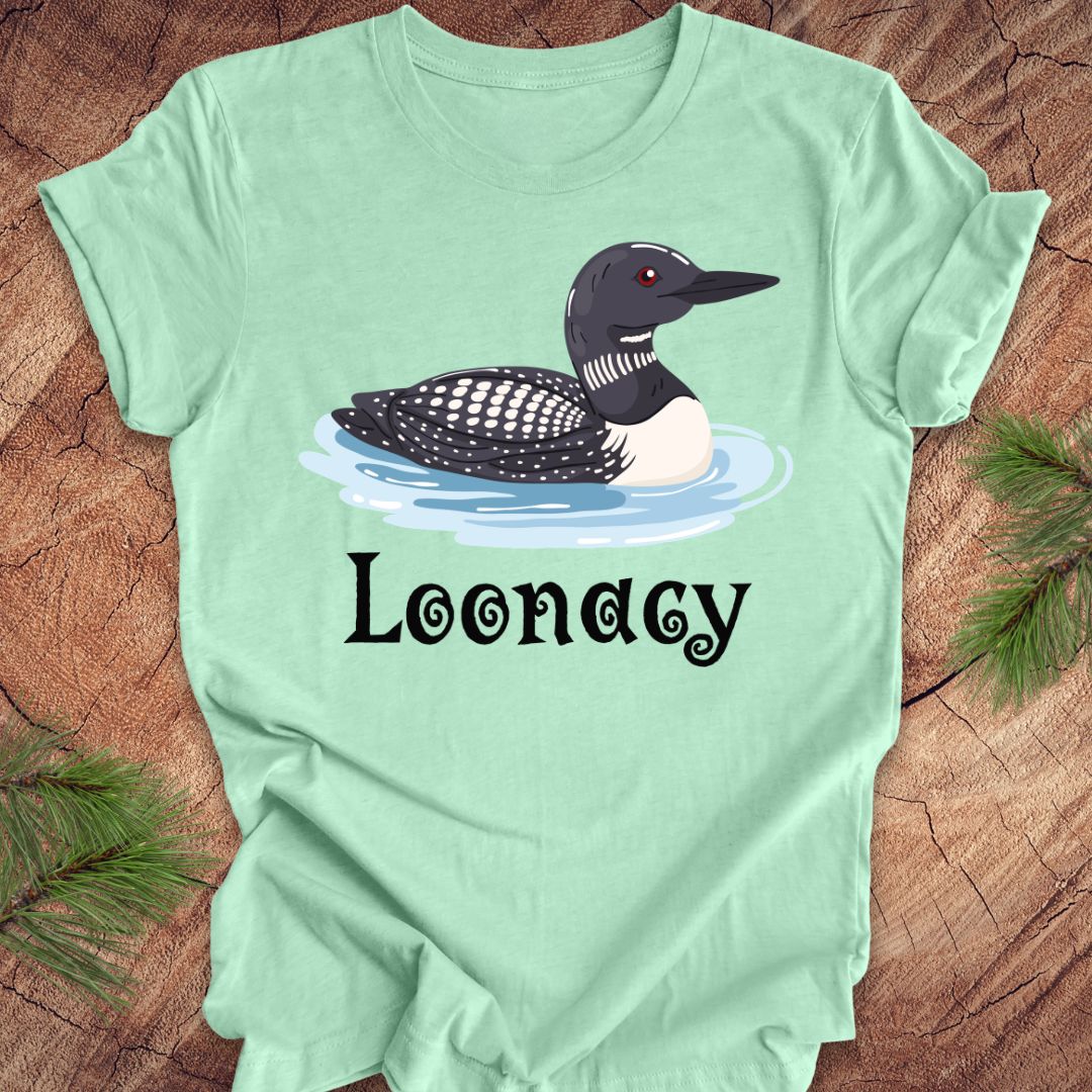 Light green t-shirt with a loon graphic and 'Loonacy' text on a wooden surface.