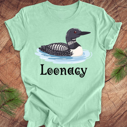 Light green t-shirt with a loon graphic and 'Loonacy' text on a wooden surface.
