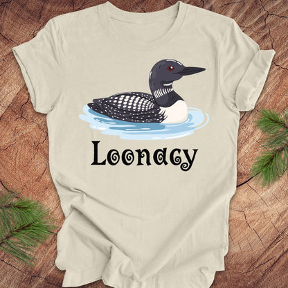 Beige t-shirt with a loon graphic and 'Loonacy' text on a wooden surface.