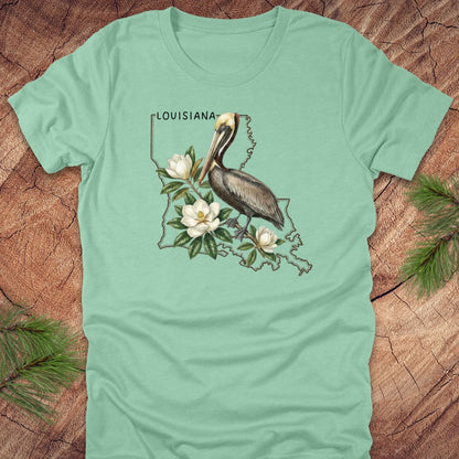 Light green t-shirt with Louisiana-themed design featuring a pelican and magnolias on a wooden surface.