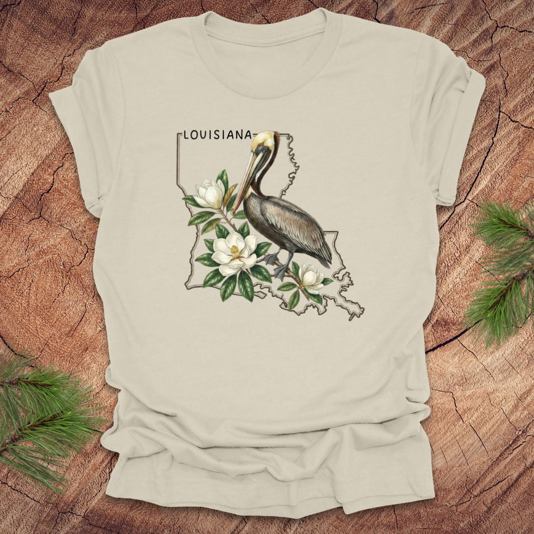 Beige t-shirt with Louisiana-themed design featuring a pelican and magnolias on a wooden surface.
