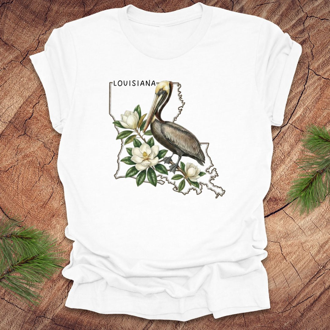 White t-shirt with Louisiana-themed design featuring a pelican and magnolias on a wooden surface.
