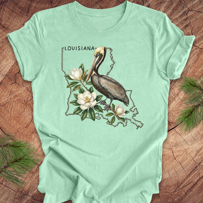 Mint green t-shirt with Louisiana-themed design featuring a pelican and magnolias on a wooden surface.
