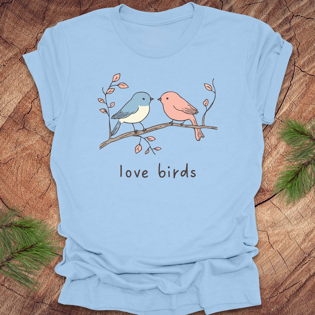 Baby blue t-shirt with a blue and a pink hand drawn bird, on a branch, with text 'love birds' on a wooden background.