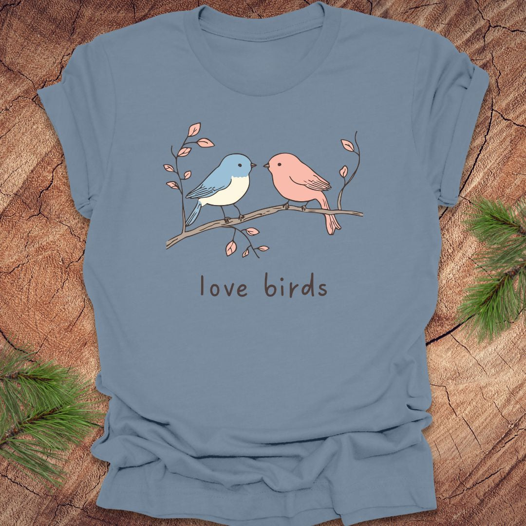 Steel blue t-shirt with a blue and a pink hand drawn bird, on a branch, with text 'love birds' on a wooden background.