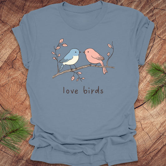 Steel blue t-shirt with a blue and a pink hand drawn bird, on a branch, with text 'love birds' on a wooden background.