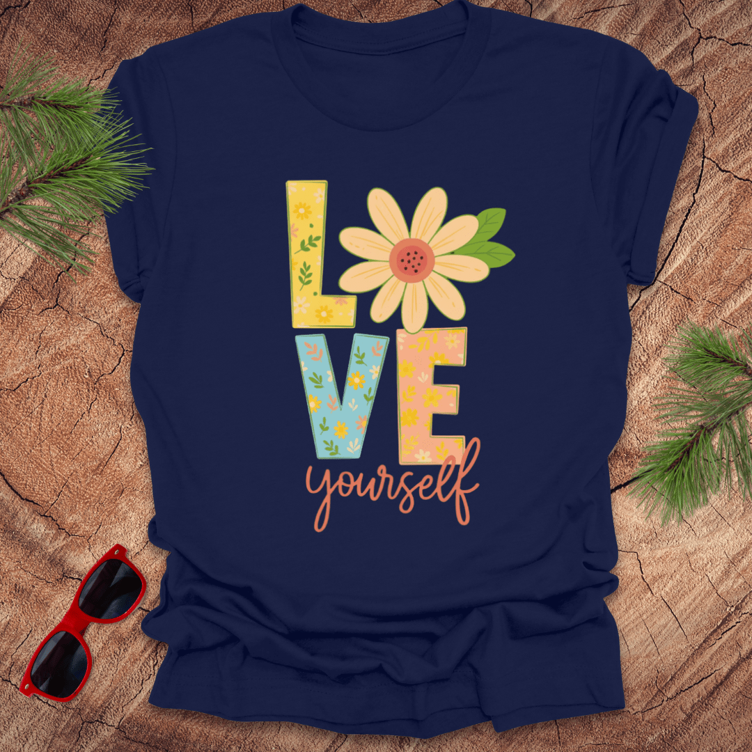 Navy blue t-shirt with 'LOVE yourself' design on a wooden surface with sunglasses and greenery.