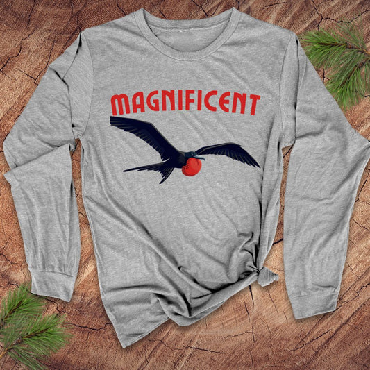 Light gray long-sleeve shirt with a frigatebird graphic and 'MAGNIFICENT' text on a wooden surface.