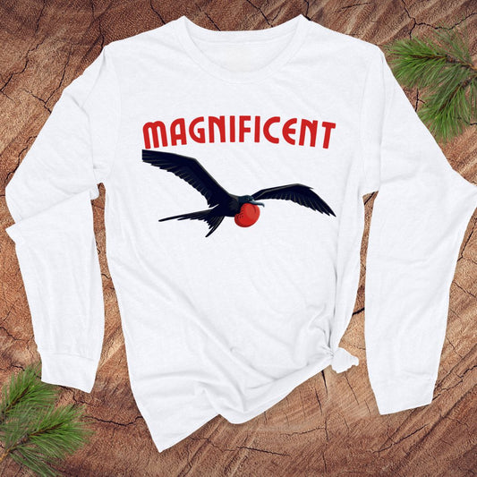White long-sleeve shirt with a frigatebird graphic and 'MAGNIFICENT' text on a wooden surface.