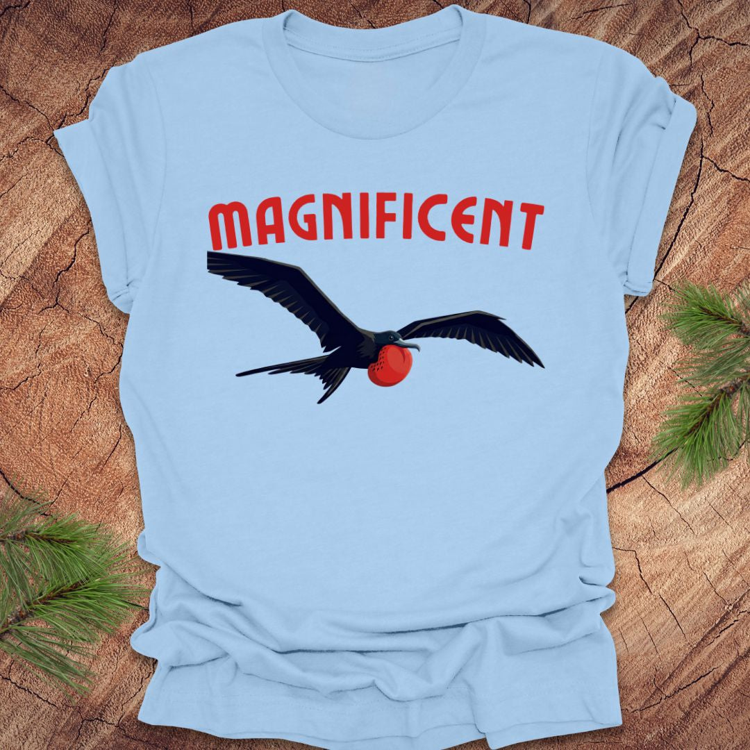 Light blue t-shirt with a bird graphic and 'MAGNIFICENT' text on a wooden surface.