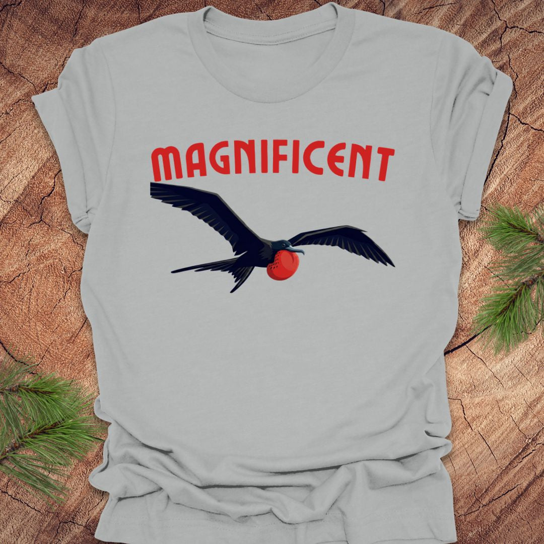 Gray t-shirt with a bird graphic and 'MAGNIFICENT' text on a wooden surface.