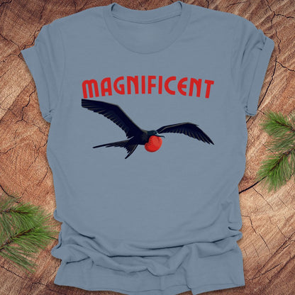 Blue t-shirt with a bird graphic and 'MAGNIFICENT' text on a wooden surface.