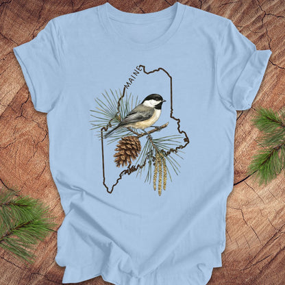 Light blue t-shirt with a chickadee and maine state outline design on a wooden surface