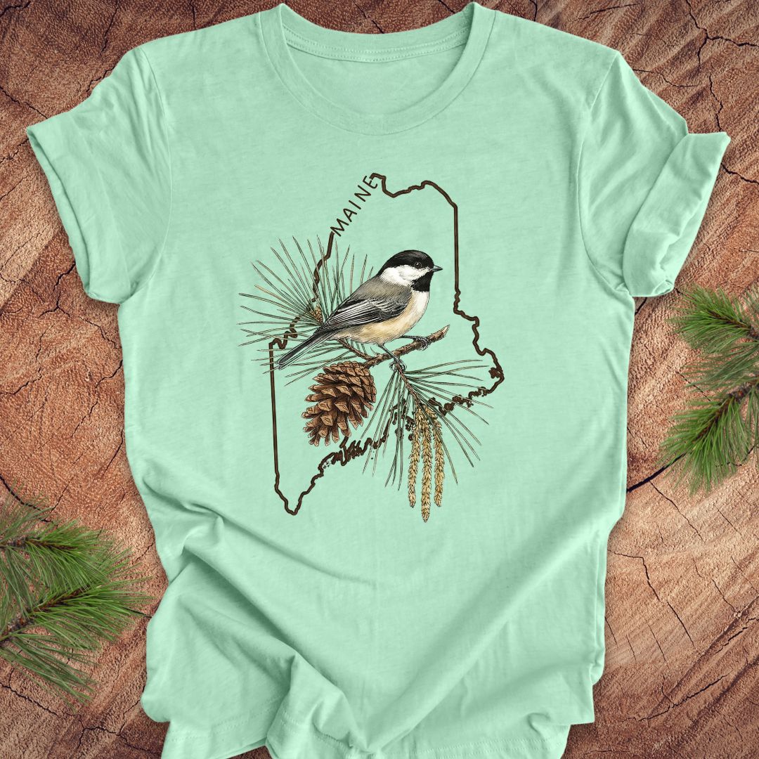 Mint green t-shirt with a chickadee and maine state outline design on a wooden surface