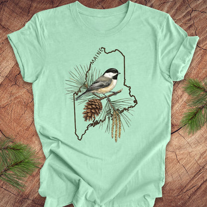 Mint green t-shirt with a chickadee and maine state outline design on a wooden surface