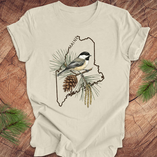 Beige t-shirt with a chickadee and maine state outline design on a wooden surface
