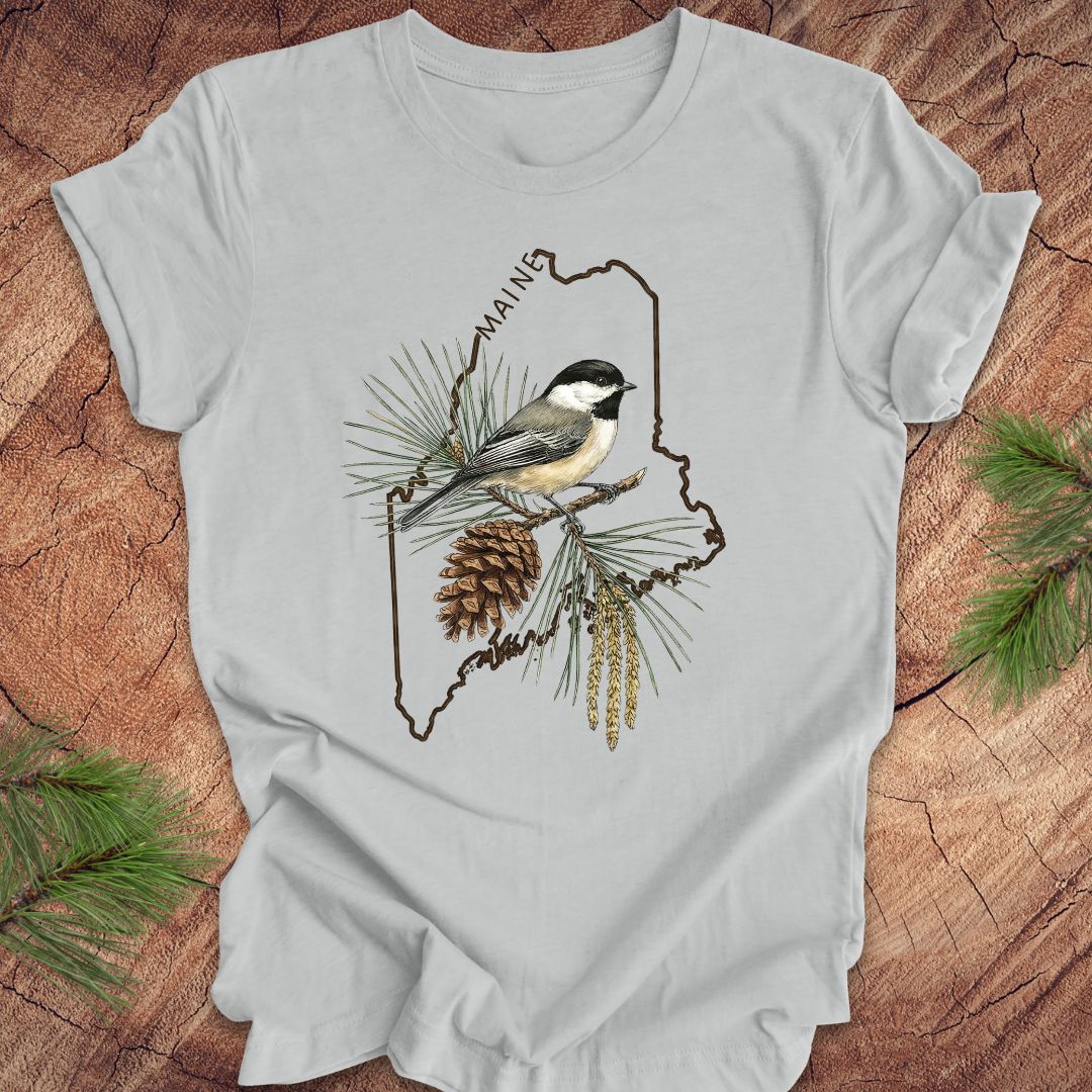 Gray t-shirt with a chickadee and maine state outline design on a wooden surface