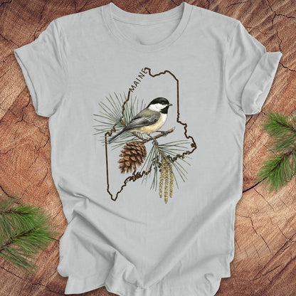 Gray t-shirt with a chickadee and maine state outline design on a wooden surface