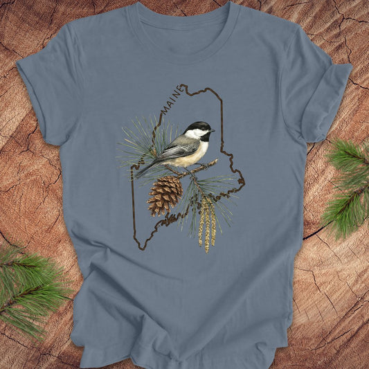 Blue t-shirt with a chickadee and maine state outline design on a wooden surface