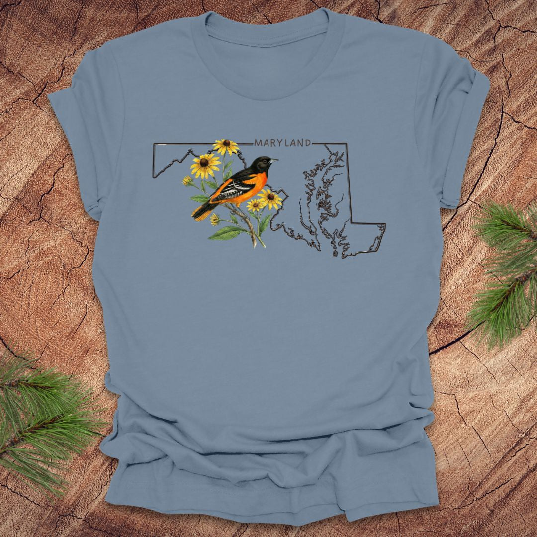 Steel blue t-shirt with Maryland state outline featuring a baltimore oriole and black eyed susans on a wooden surface