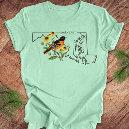 Light green t-shirt with Maryland design featuring a bird and flowers on a wooden surface.