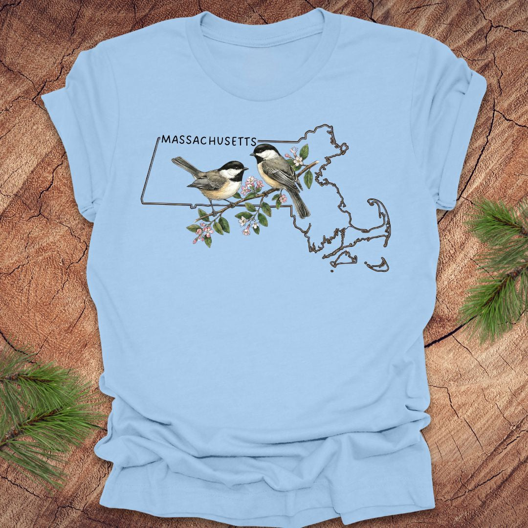Baby blue t-shirt with Massachusetts map and chickadee design on a wooden surface