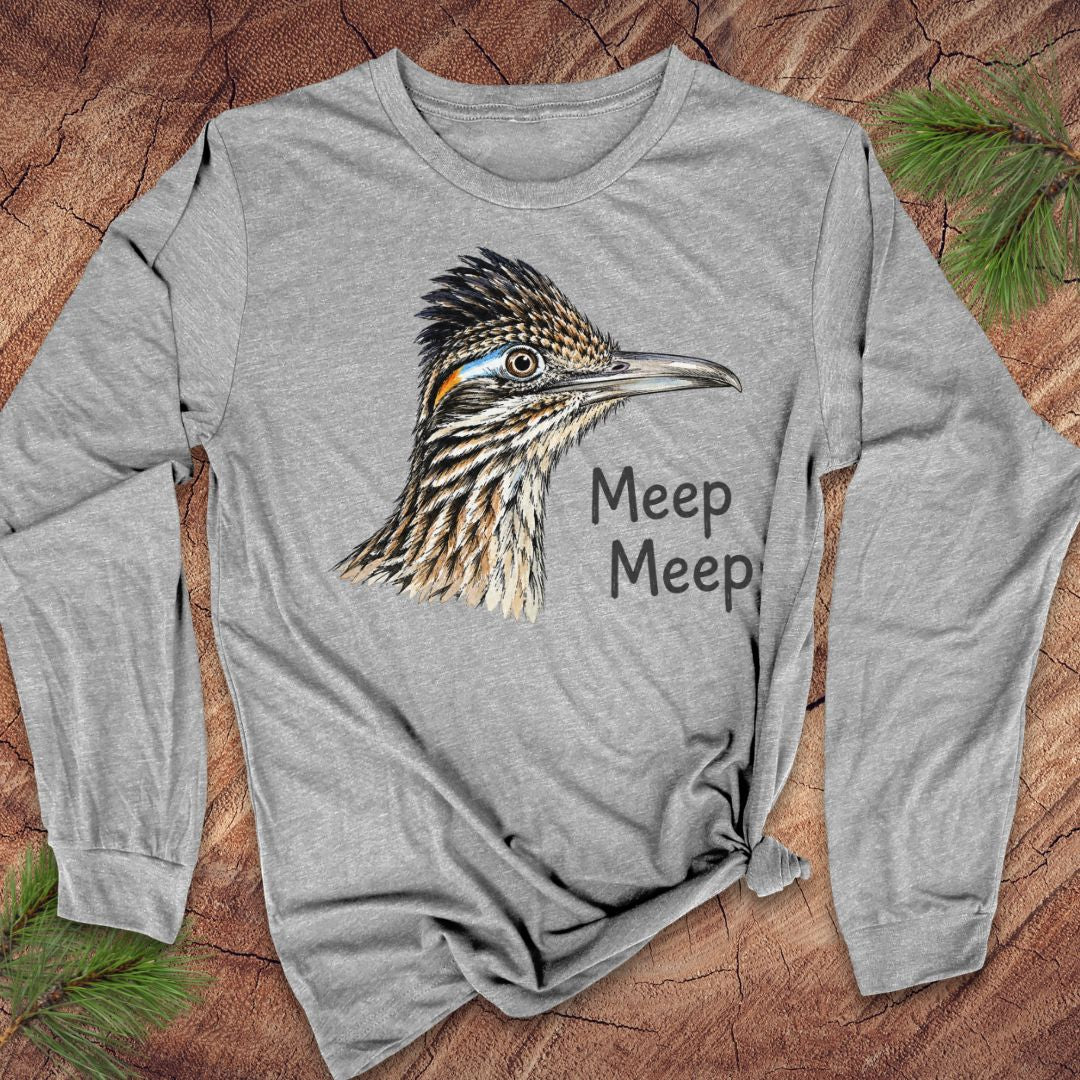 A heather gray long-sleeve t-shirt featuring a detailed graphic of a roadrunner bird and the text 'Meep Meep' printed on the front, styled flat on a rustic wood background with pine needles.