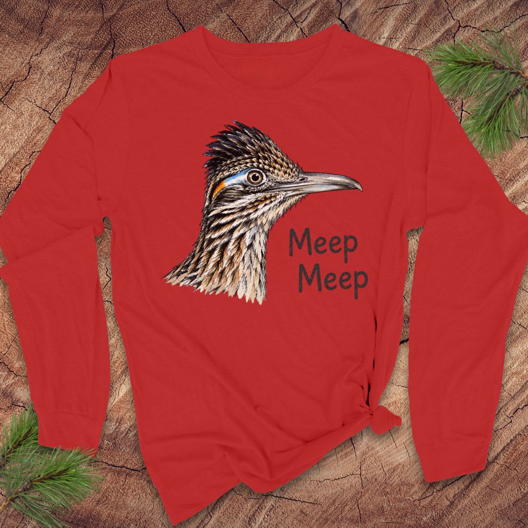 A red long-sleeve t-shirt with a detailed graphic of a roadrunner bird and the text 'Meep Meep' printed on the front, styled flat on a rustic wood background with pine needles.