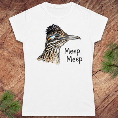 A white short-sleeve crewneck t-shirt featuring a detailed graphic of a roadrunner bird head and the text 'Meep Meep' printed in black. The t-shirt is displayed flat on a textured brown wood background with green pine needles in the corners.