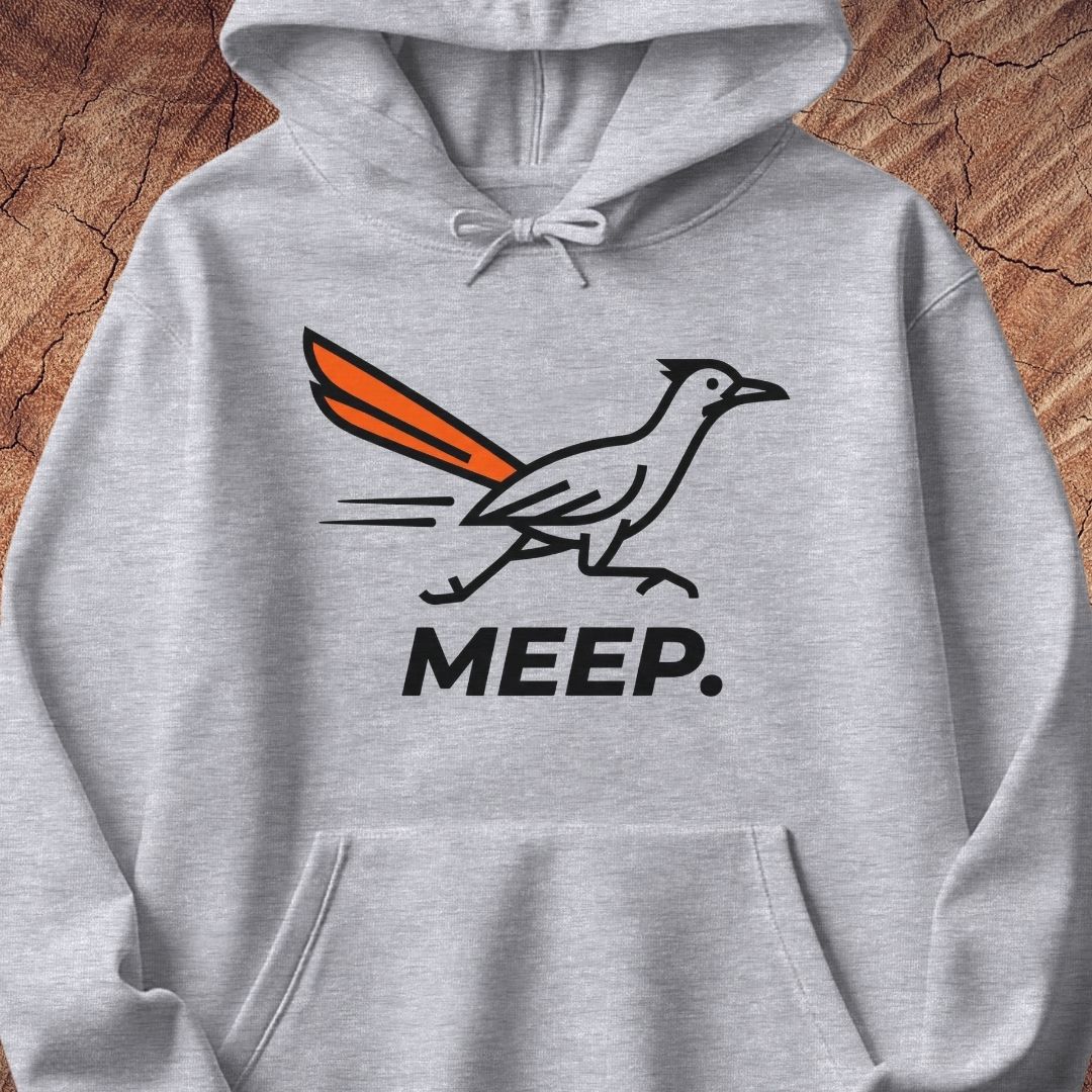 A light heather gray pullover hoodie featuring a graphic of a roadrunner with an orange tail and the word 'MEEP.' printed below in black, displayed against a rustic wood background.