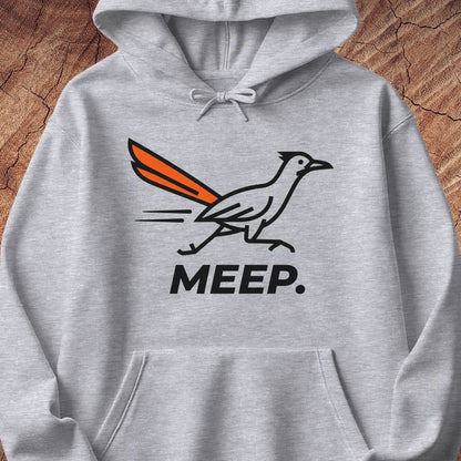 A light heather gray pullover hoodie featuring a graphic of a roadrunner with an orange tail and the word 'MEEP.' printed below in black, displayed against a rustic wood background.