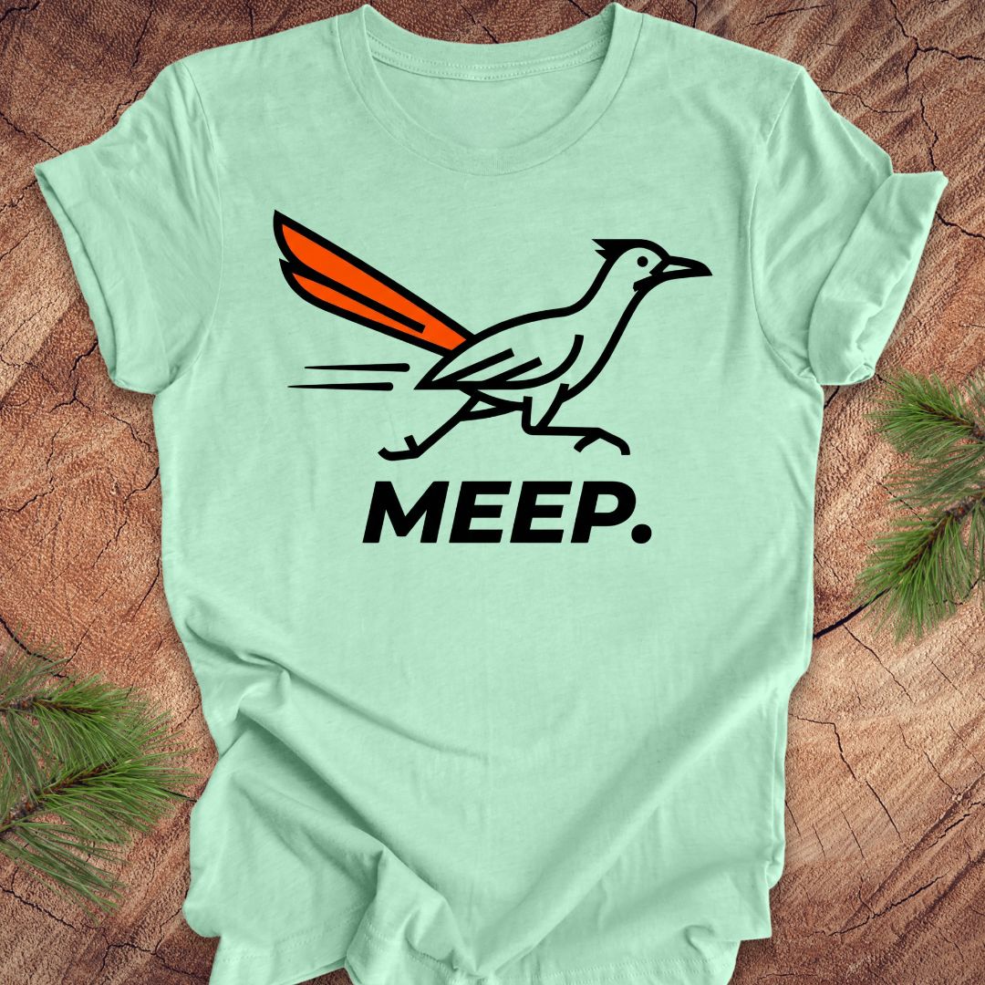 Mint green t-shirt with a graphic of a roadrunner and 'MEEP.' text on a wooden surface.