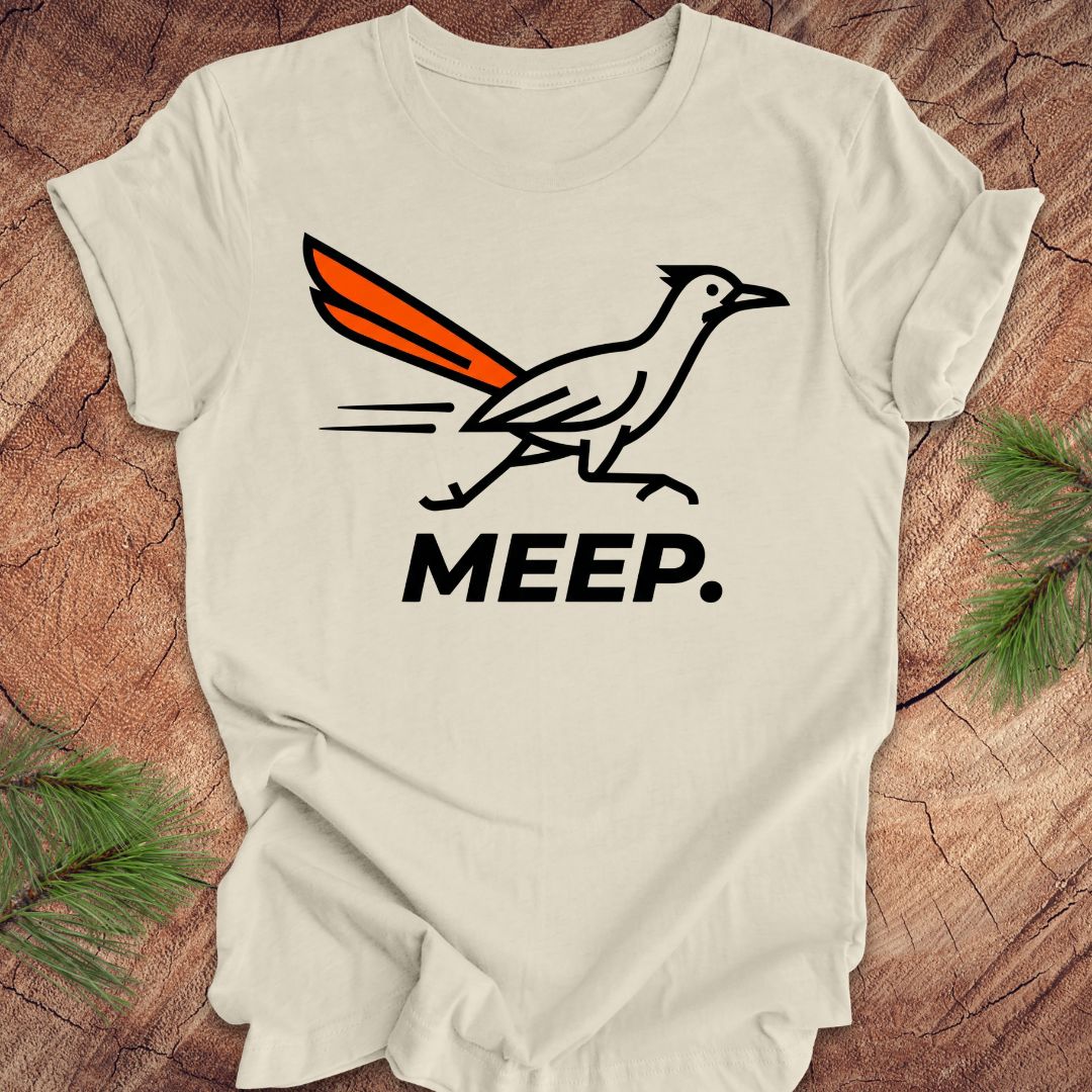 Beige t-shirt with a graphic of a roadrunner and 'MEEP.' text on a wooden surface.