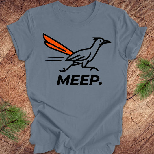 Blue t-shirt with a graphic of a roadrunner and 'MEEP.' text on a wooden surface.