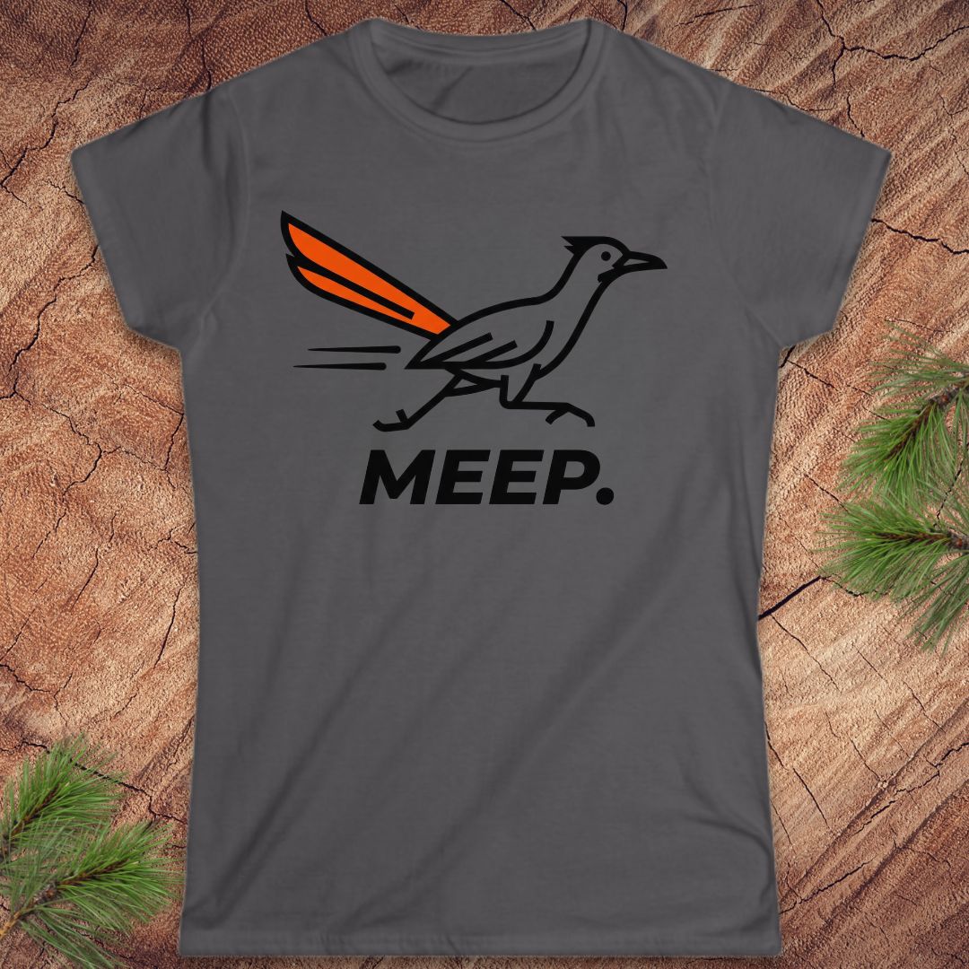 A dark gray short-sleeve t-shirt with a graphic of a roadrunner bird with an orange tail and the word 'MEEP.' printed below it, displayed flat on a rustic wood background with pine branches.
