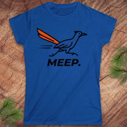 A royal blue short-sleeve t-shirt with a graphic of a roadrunner and the word 'MEEP.' printed on the front, displayed flat on a rustic wood background with pine needles.