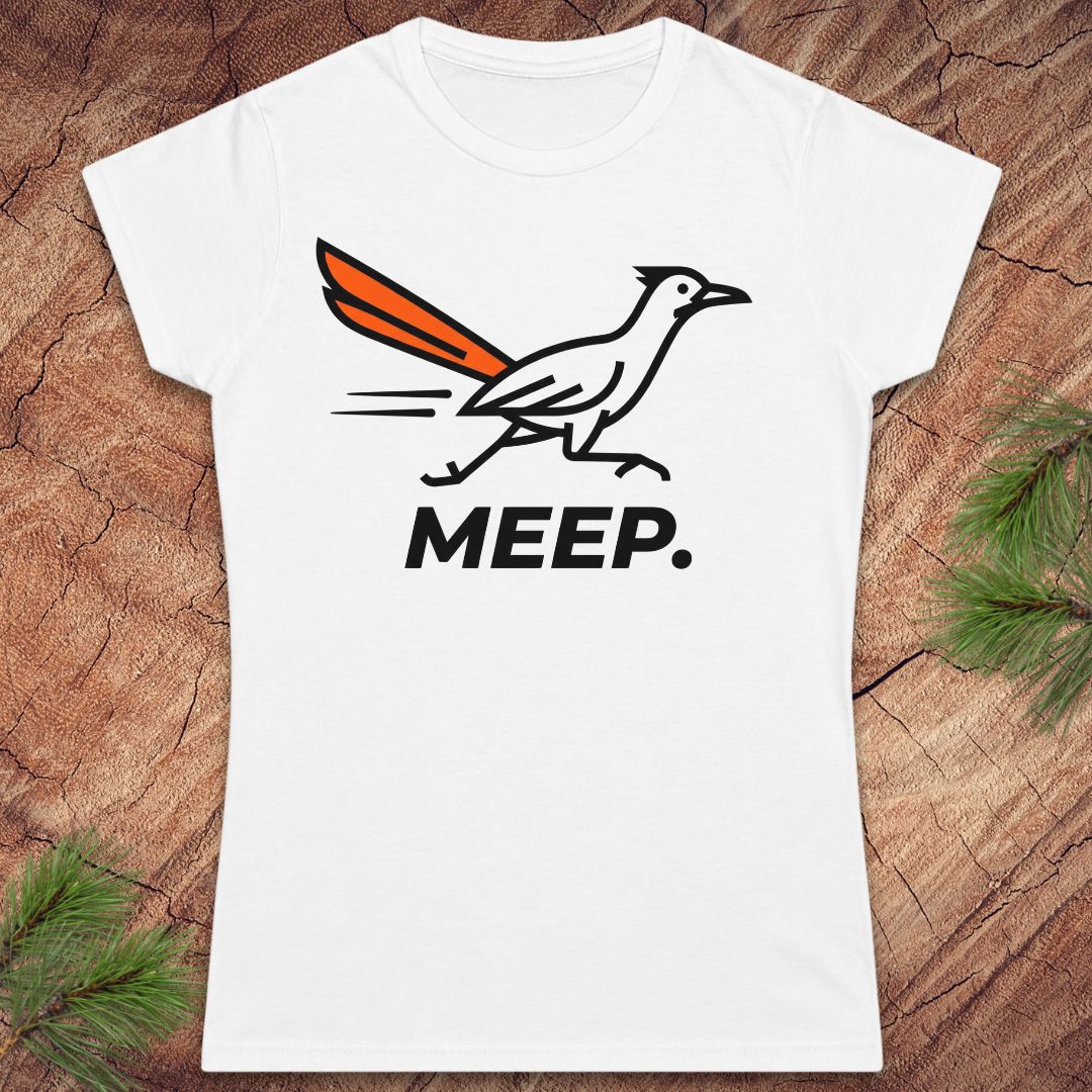 A white short-sleeve crewneck t-shirt featuring a roadrunner graphic with an orange tail and the word 'MEEP.' printed below it, displayed flat on a rustic wood background with pine branches in the corners.