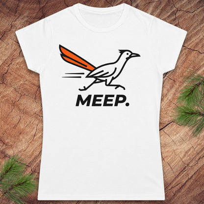 A white short-sleeve crewneck t-shirt featuring a roadrunner graphic with an orange tail and the word 'MEEP.' printed below it, displayed flat on a rustic wood background with pine branches in the corners.