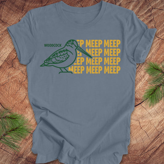 Blue t-shirt with a green woodcock graphic and yellow 'meep' text on a wooden surface.