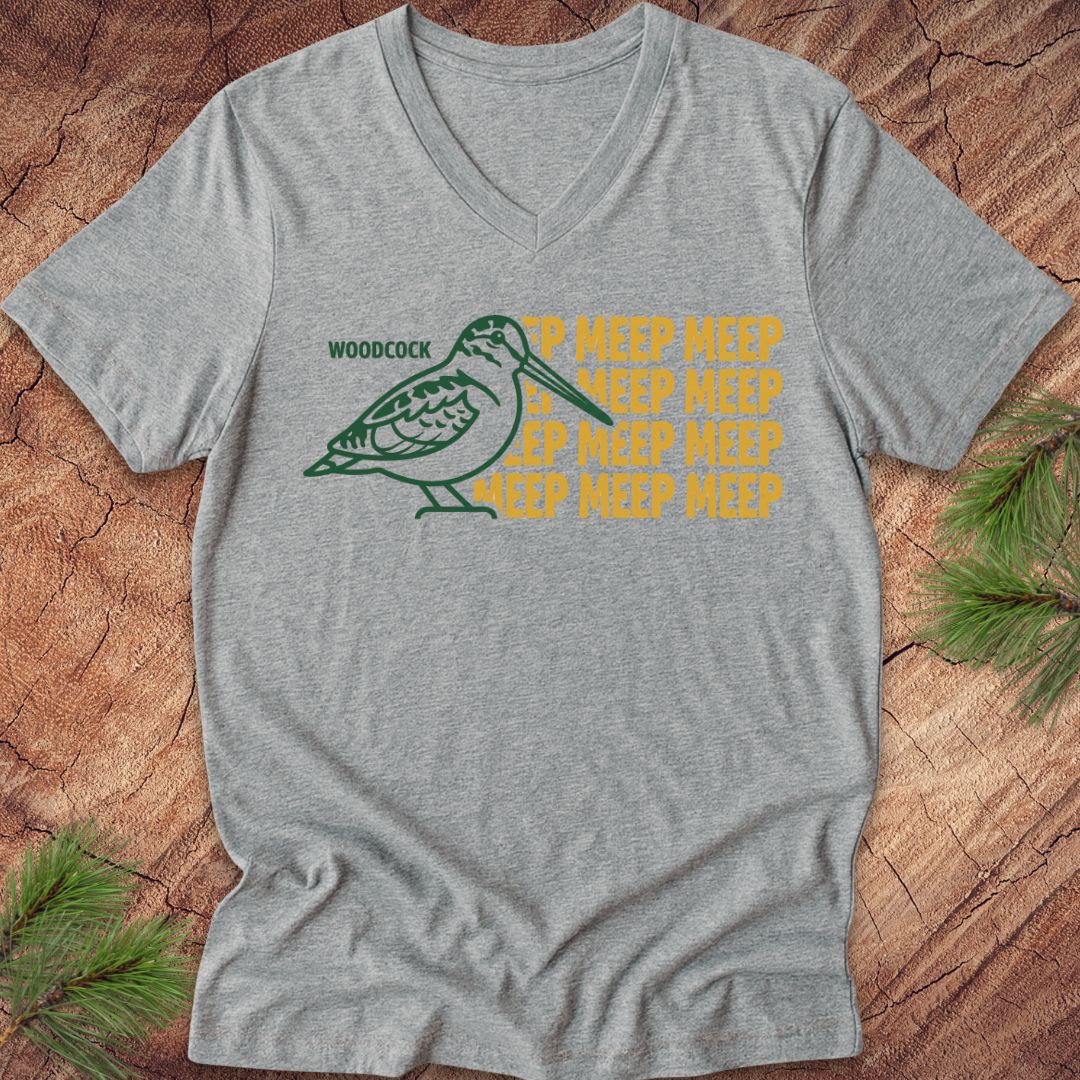 Gray v-neck t-shirt with a green woodcock design and yellow text on a wooden surface.
