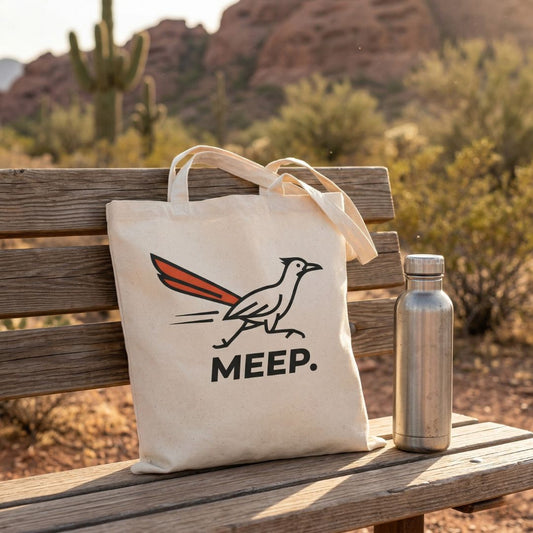 Tote bag with 'MEEP.' roadrunner design on a wooden bench in a desert setting