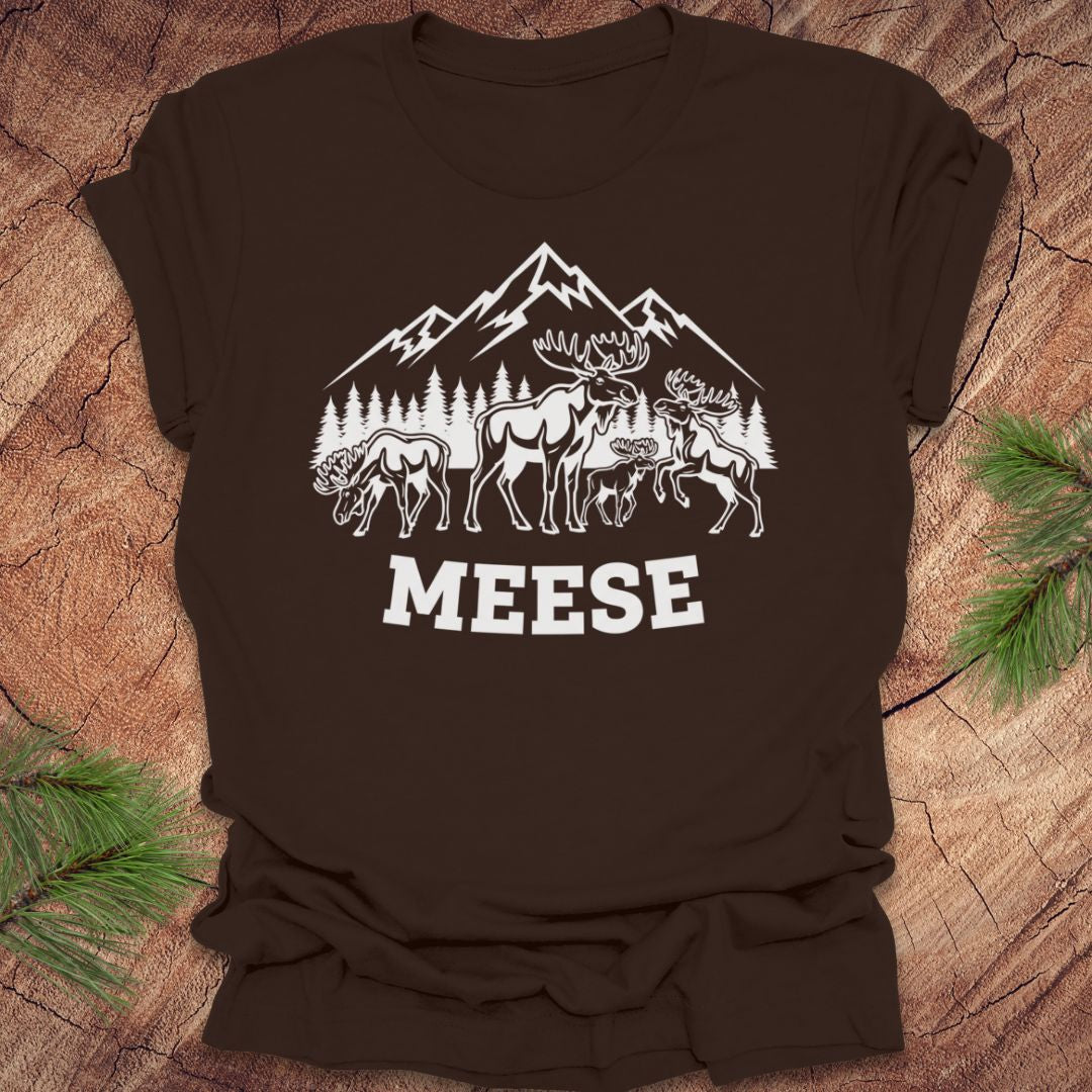 Brown t-shirt with moose, trees and mountains with text "meese"on a wood background. 