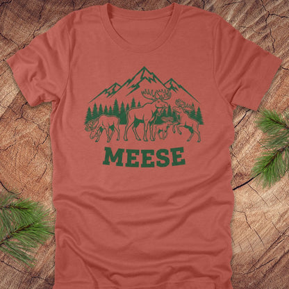 Clay colored t-shirt with moose, trees and mountains with text "meese"on a wood background. 