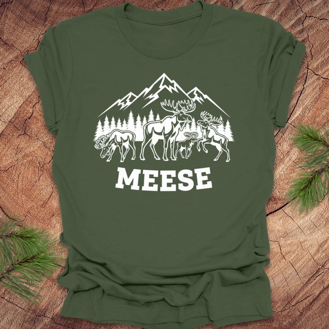 Green t-shirt with moose, trees and mountains with text "meese"on a wood background. 