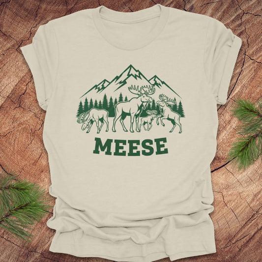 Beige t-shirt with moose, trees and mountains with text "meese"on a wood background. 