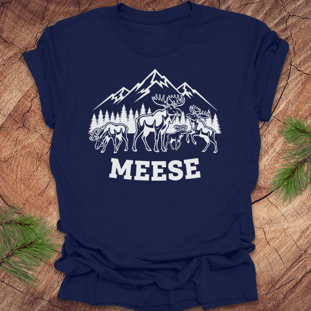 Navy blue t-shirt with moose, trees and mountains with text "meese"on a wood background. 